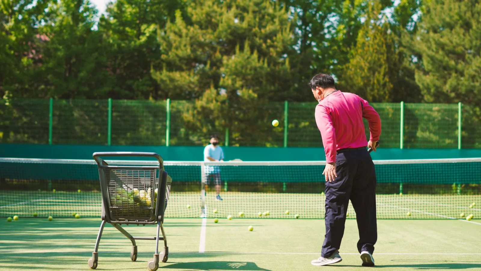 Tennistrainer voert een training met een ballenkar op de baan